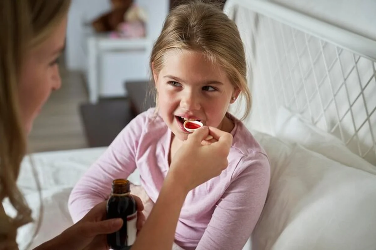 Matka podaje syrop chorej dziewczynie w łóżku
