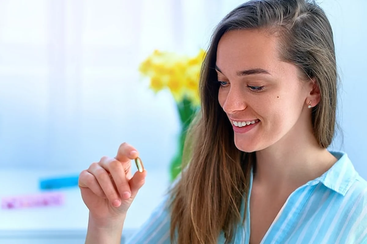 Młoda kobieta biorąca suplement diety witaminę omega 3 i D w formie miękkich żeli