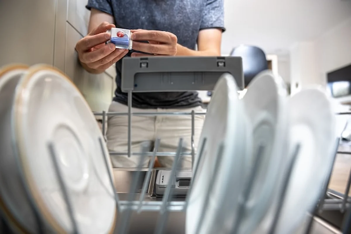 Mężczyzna trzyma tabletę do mycia naczyń w otwartej zmywarce