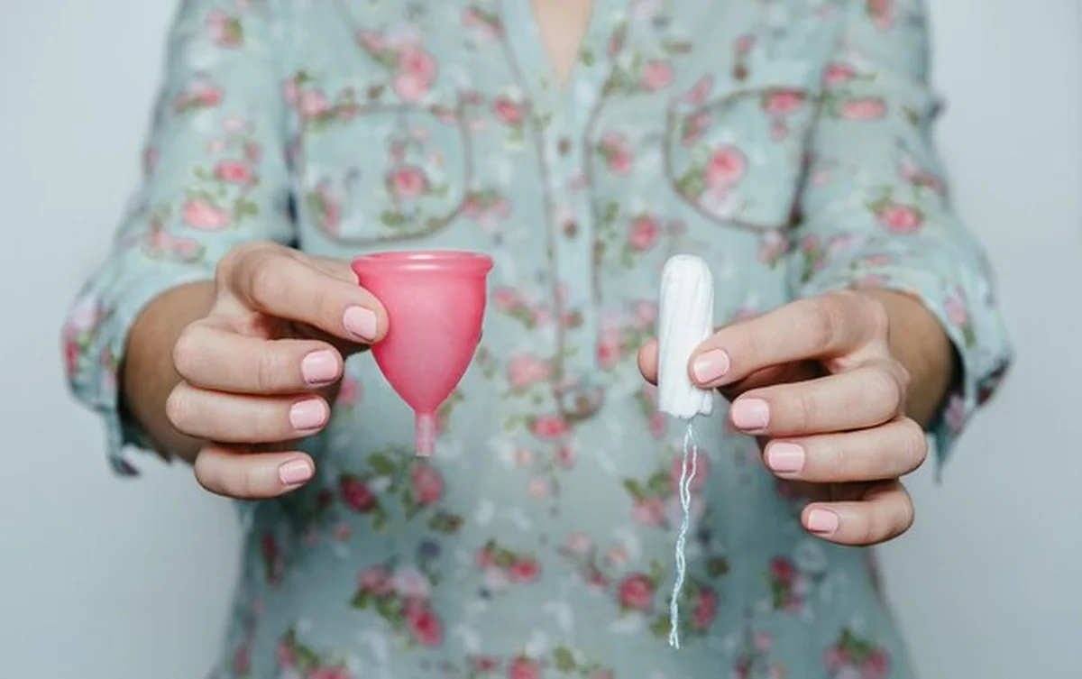 Ręce kobiety trzymające menstruacyjny kubek i tampon. Różne metody higieny intymnej