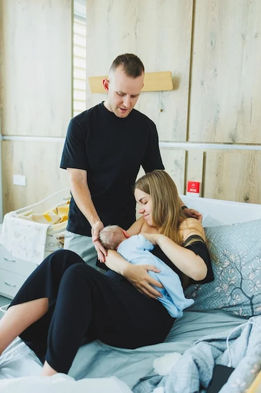 Młoda matka i ojciec uściskują nowo narodzonego syna, kobieta karmi dziecko piersią