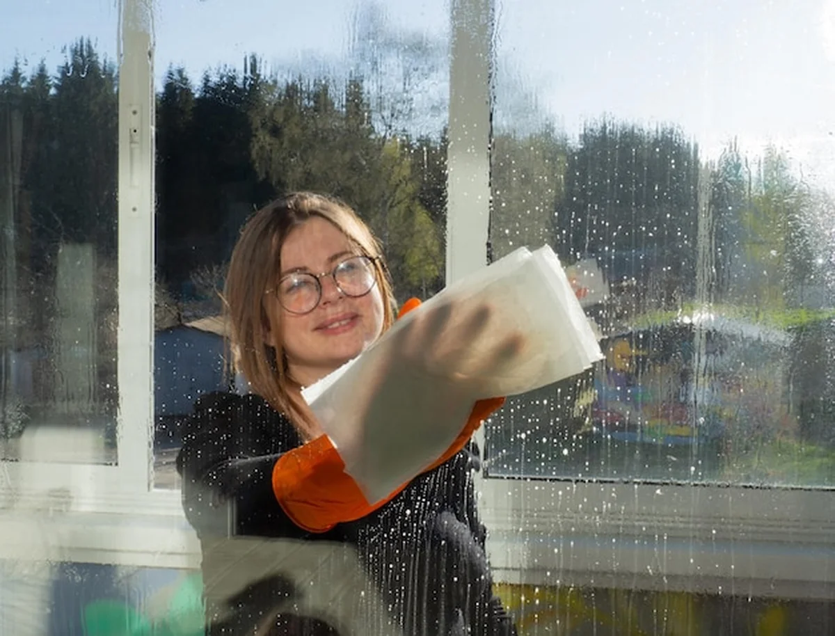 Młoda dziewczyna myjąca okna szmatką i spryskująca szyby