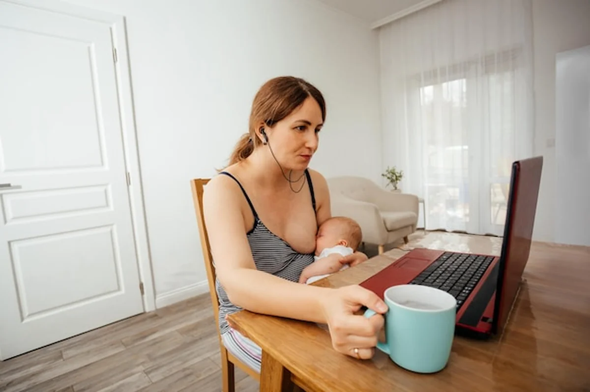 Matka karmiąca piersią dziecko przy laptopie w domu