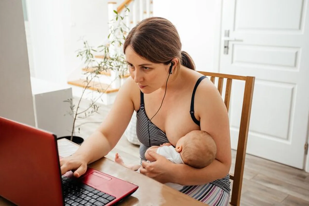 Matka karmiąca piersią dziecko przy laptopie w domu
