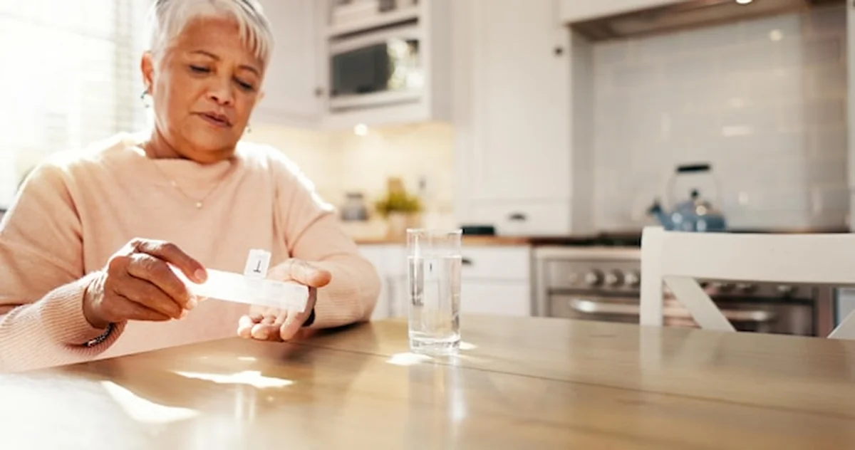 Starsza kobieta pije wodę i leki w domu