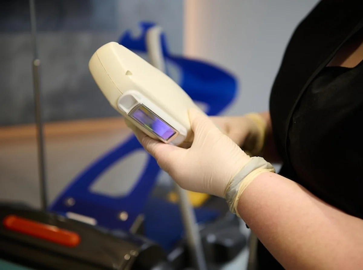 Nowoczesna aparatura do depilacji laserowej i ręce kosmetyczki w rękawiczkach medycznych